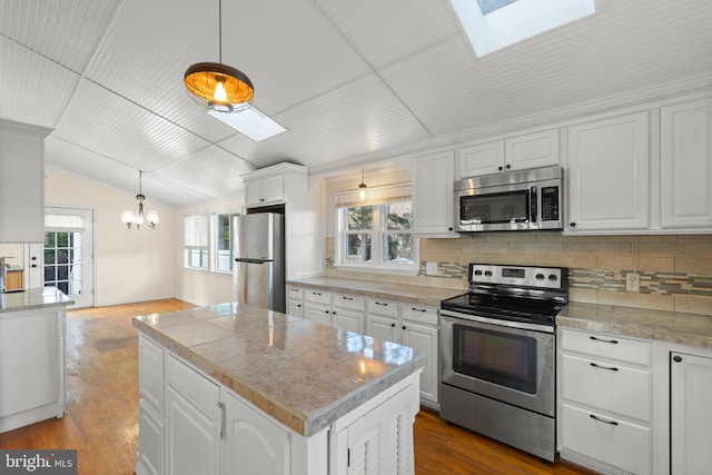 kitchen featuring hanging light fixtures, a kitchen island, white cabinets, and appliances with stainless steel finishes