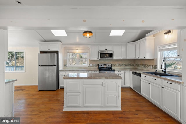 kitchen featuring sink, white cabinetry, a skylight, stainless steel appliances, and a center island