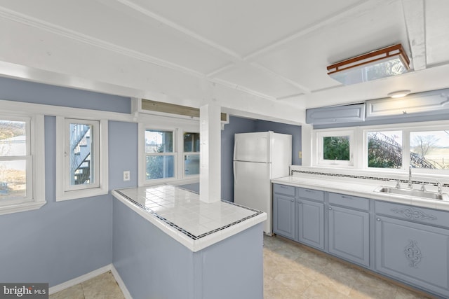 kitchen featuring white refrigerator, tile counters, kitchen peninsula, and sink