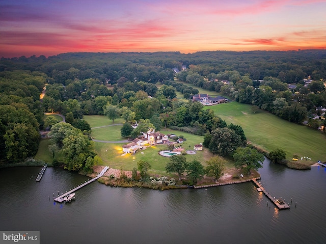 aerial view at dusk with a water view and a view of trees