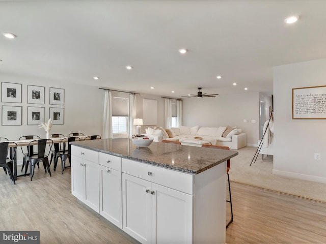 kitchen featuring dark stone counters, light wood-type flooring, a center island, white cabinetry, and a kitchen breakfast bar