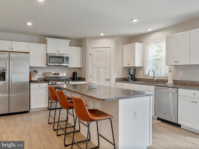 kitchen with white cabinets, sink, a kitchen island, light hardwood / wood-style flooring, and stainless steel appliances