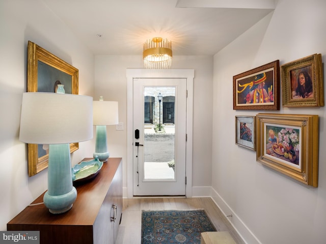 doorway featuring a healthy amount of sunlight, light wood-type flooring, baseboards, and a chandelier