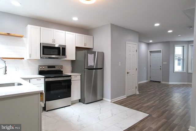 kitchen with appliances with stainless steel finishes, light hardwood / wood-style floors, tasteful backsplash, white cabinets, and sink