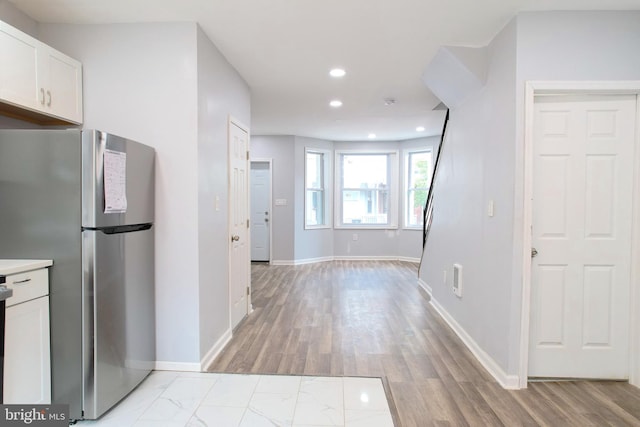 kitchen with light wood-type flooring, stainless steel refrigerator, and white cabinetry