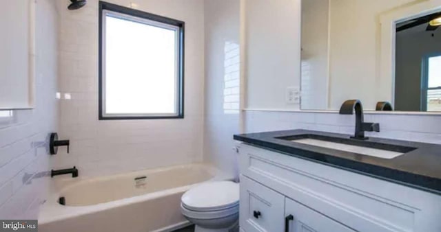 full bathroom with tiled shower / bath, vanity, toilet, and a healthy amount of sunlight