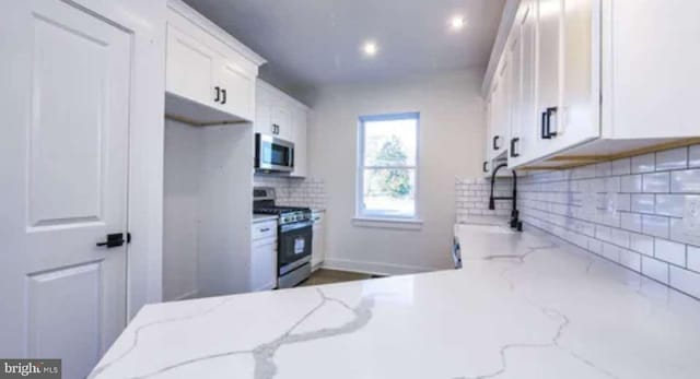 kitchen featuring sink, light stone counters, backsplash, appliances with stainless steel finishes, and white cabinetry