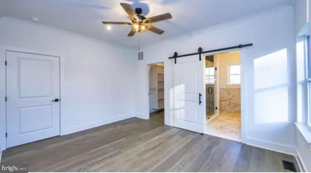 unfurnished room featuring a barn door, dark hardwood / wood-style floors, and ceiling fan