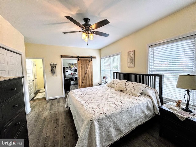 bedroom featuring connected bathroom, ceiling fan, a barn door, dark hardwood / wood-style flooring, and a closet