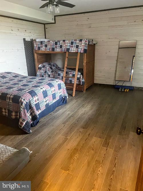 bedroom featuring ceiling fan, hardwood / wood-style floors, and wood walls