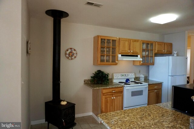 kitchen with light stone countertops, light tile patterned floors, white appliances, and a wood stove