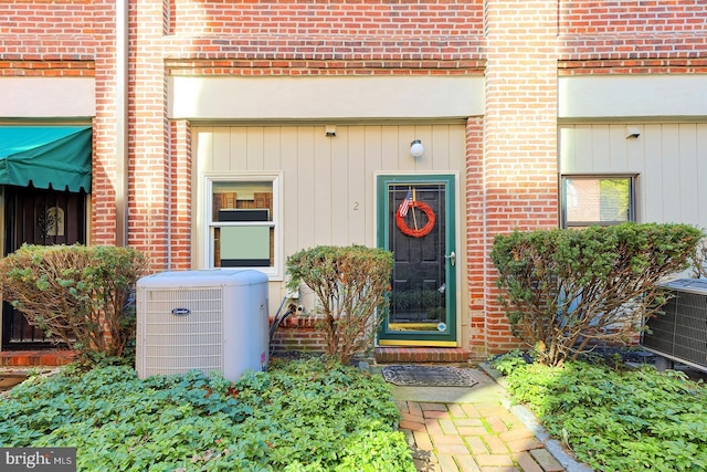 doorway to property with central air condition unit, board and batten siding, and brick siding
