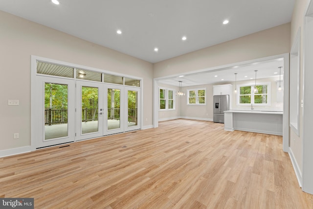 unfurnished living room with french doors, a notable chandelier, and light wood-type flooring