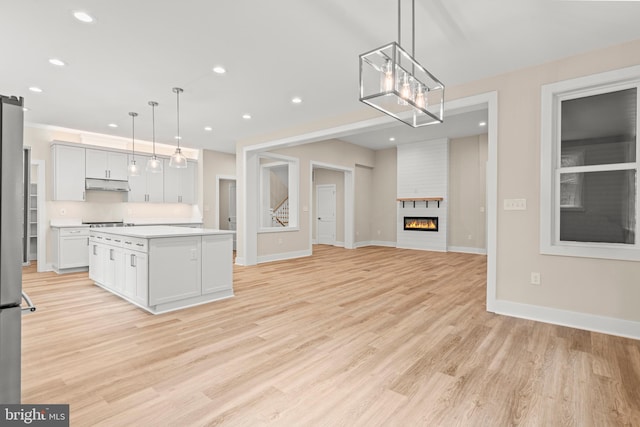 kitchen featuring a kitchen island, a large fireplace, decorative light fixtures, light wood-type flooring, and white cabinetry