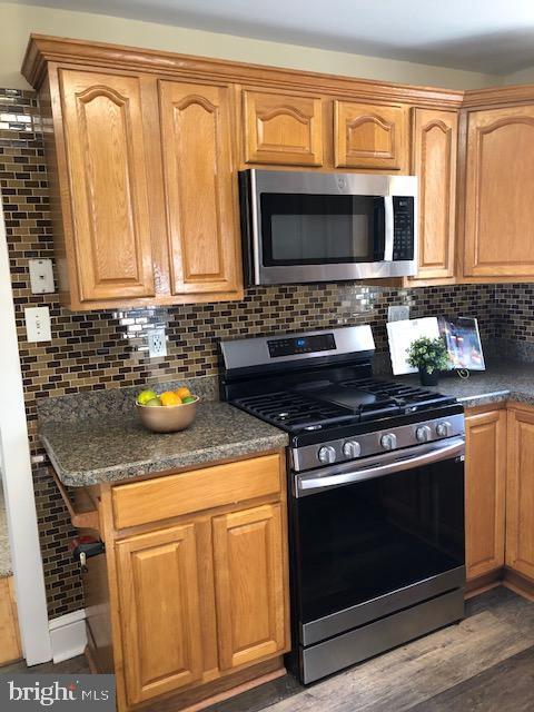 kitchen with dark stone countertops, appliances with stainless steel finishes, dark hardwood / wood-style floors, and tasteful backsplash