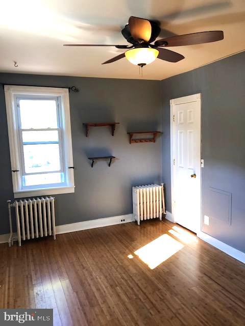 empty room featuring ceiling fan, radiator, and dark hardwood / wood-style flooring