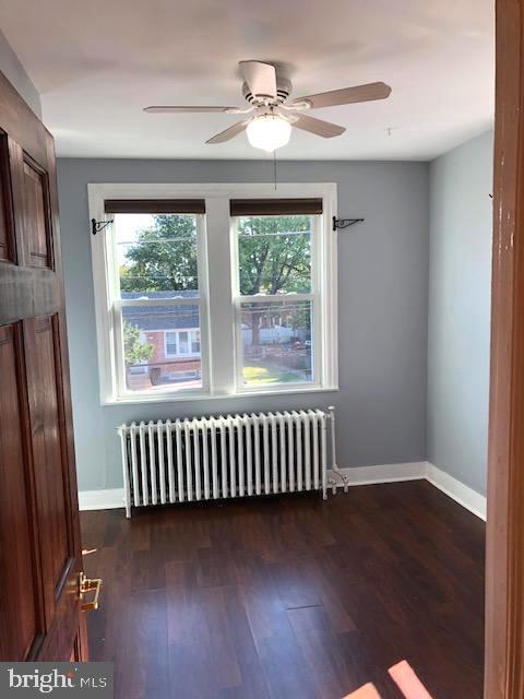 spare room featuring ceiling fan, dark hardwood / wood-style floors, and radiator heating unit