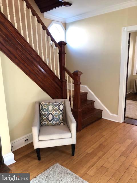 stairs featuring wood-type flooring, radiator, and crown molding