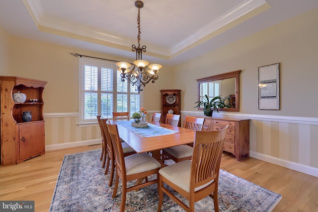 dining room featuring a notable chandelier, baseboards, ornamental molding, light wood finished floors, and a raised ceiling