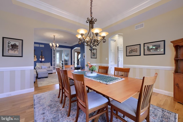 dining area featuring a notable chandelier, visible vents, crown molding, a wainscoted wall, and arched walkways