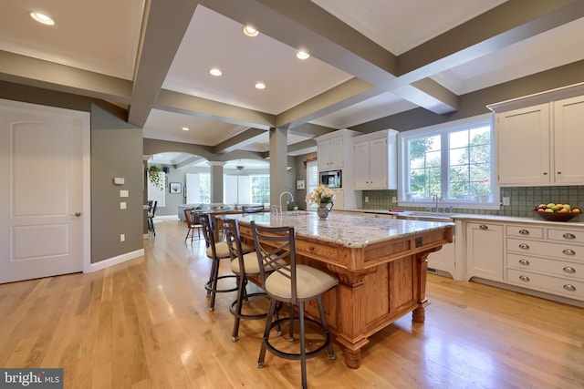 kitchen featuring coffered ceiling, stainless steel microwave, backsplash, and ornate columns