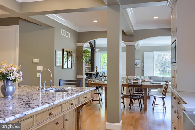 kitchen with light stone countertops, ornate columns, arched walkways, and a sink