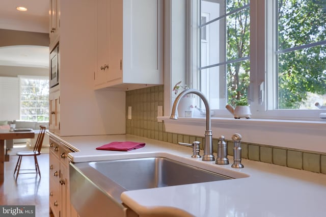 kitchen with built in microwave, a sink, white cabinetry, decorative backsplash, and light countertops