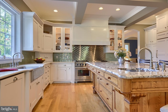 kitchen with white cabinetry, high end range, crown molding, and a sink