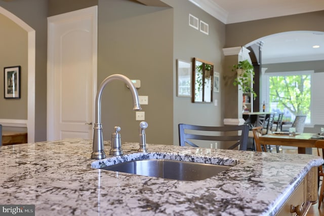 kitchen featuring a sink, crown molding, visible vents, arched walkways, and light stone counters