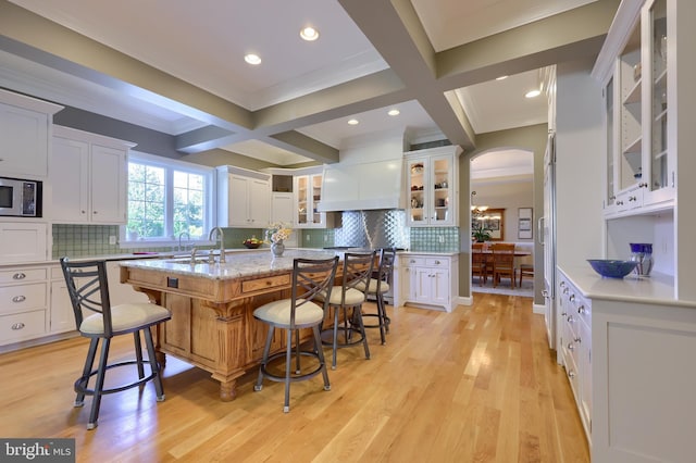 kitchen with an island with sink, white cabinetry, arched walkways, and a breakfast bar area