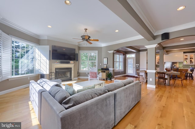 living room with decorative columns, a fireplace with flush hearth, light wood-type flooring, baseboards, and ceiling fan