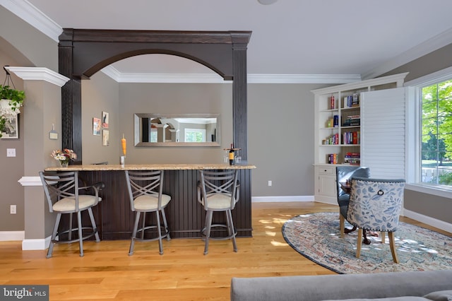 kitchen with a breakfast bar area, wood finished floors, baseboards, arched walkways, and ornamental molding