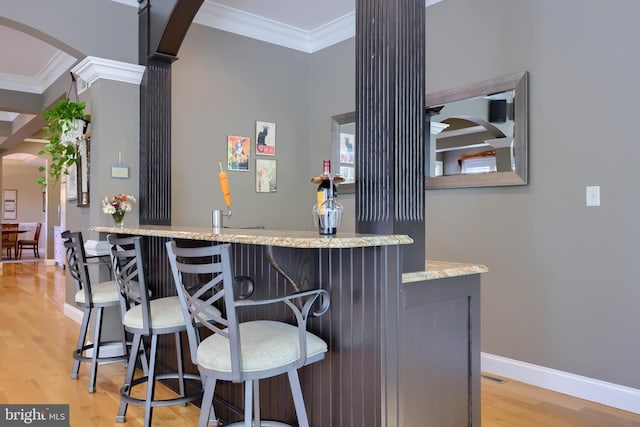 bar featuring crown molding, a community bar, decorative columns, and arched walkways