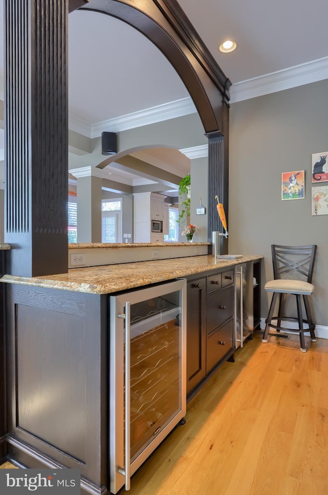 bar with ornamental molding, arched walkways, light wood-style flooring, and beverage cooler