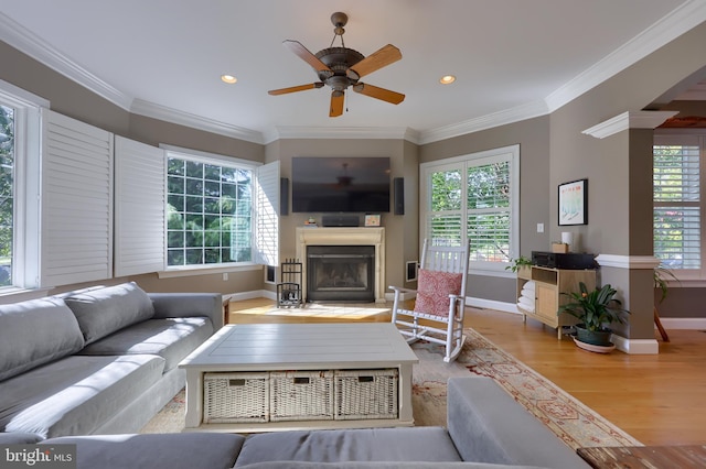 living room with recessed lighting, a fireplace with raised hearth, baseboards, crown molding, and wood finished floors