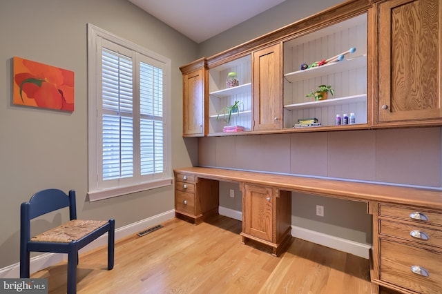 office space featuring light wood finished floors, built in desk, and visible vents