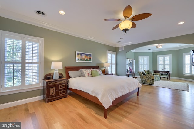 bedroom with arched walkways, baseboards, crown molding, and light wood-style floors