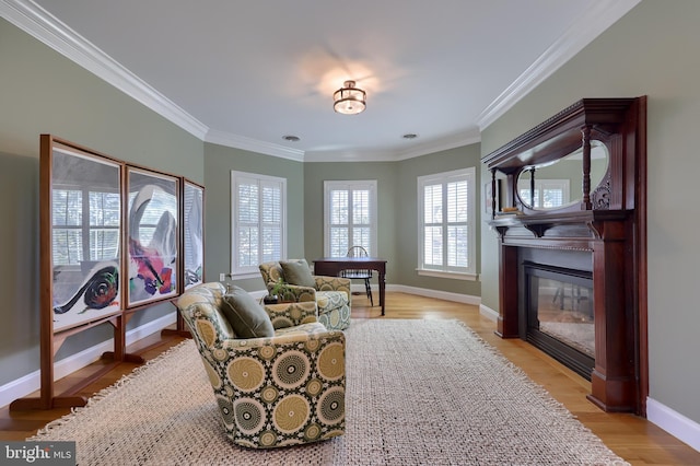 living area featuring light wood finished floors, baseboards, ornamental molding, and a glass covered fireplace