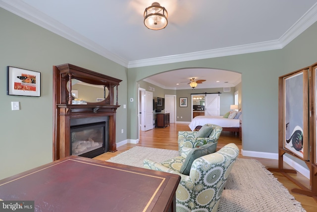 bedroom featuring baseboards, ornamental molding, light wood finished floors, a glass covered fireplace, and arched walkways