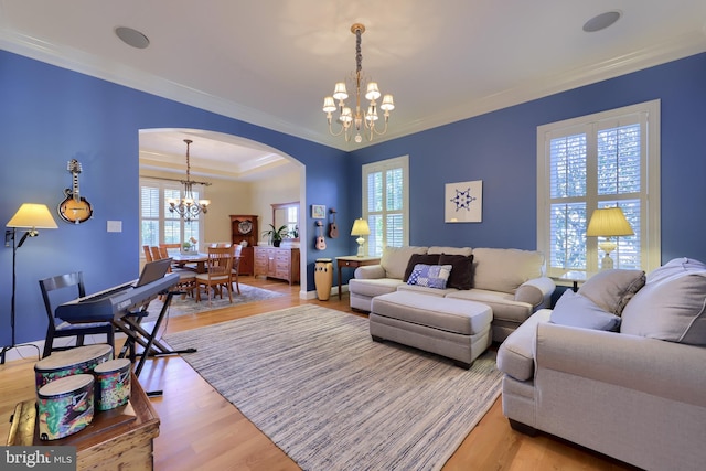 living area with ornamental molding, light wood-type flooring, an inviting chandelier, arched walkways, and a tray ceiling