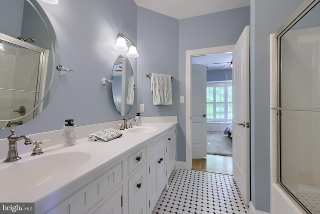 bathroom with a sink, a shower with shower door, double vanity, and a ceiling fan