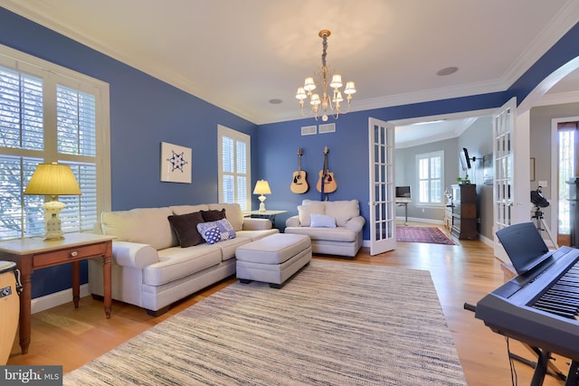 living room featuring baseboards, arched walkways, light wood-style floors, a chandelier, and ornamental molding