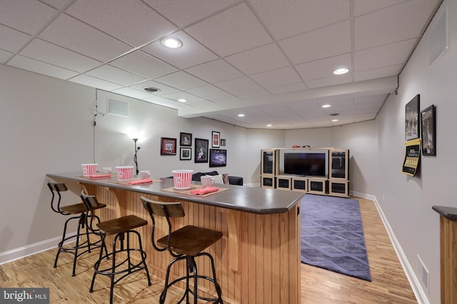bar with baseboards, a drop ceiling, visible vents, and light wood-type flooring