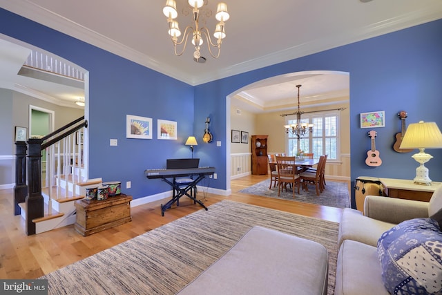 living area featuring wood finished floors, a notable chandelier, crown molding, arched walkways, and stairs