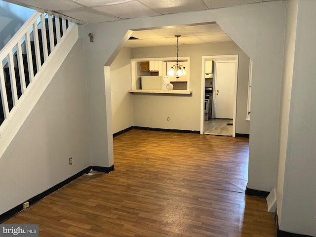 unfurnished living room featuring a drop ceiling, dark hardwood / wood-style floors, and an inviting chandelier