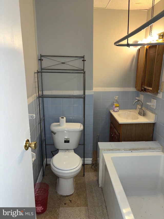 bathroom featuring vanity, a bathtub, tile patterned floors, tile walls, and toilet