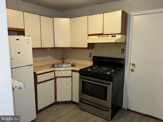 kitchen with white refrigerator, sink, tasteful backsplash, stainless steel range with gas stovetop, and light wood-type flooring