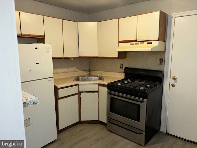 kitchen featuring light wood-type flooring, stainless steel gas stove, white fridge, and sink