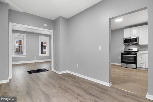 interior space with white cabinetry, light hardwood / wood-style floors, tasteful backsplash, and appliances with stainless steel finishes