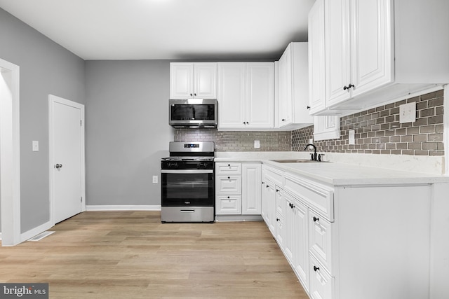 kitchen with light hardwood / wood-style floors, appliances with stainless steel finishes, sink, and white cabinets